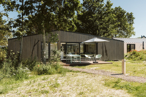 Moderne lodge in vakantiepark De Klepperstee in Nederland, met houten gevel, terras en parasol.