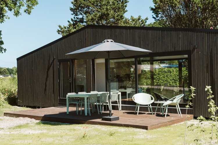 Moderne Terrasse mit Gartenmöbeln und Sonnenschirm vor der Eden Lodge im Ferienpark De Klepperstee, Niederlande.