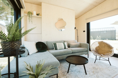 Lichte, moderne woonkamer in Eden-lodge van Holiday park De Klepperstee, met planten en hoekbank.