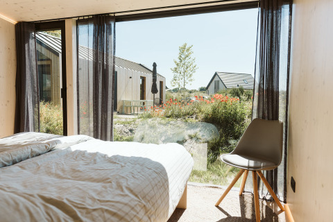 Bedroom view inside Eden lodge at Holiday Park De Klepperstee, Netherlands, overlooking gardens and cabins.