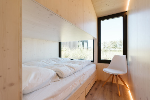 Stanza minimalista in legno con letto comodo e sedia bianca a Eden, Holiday park De Klepperstee, Paesi Bassi.