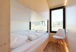Habitación de madera luminosa con cama individual y silla blanca en Eden, Holiday park De Klepperstee, Países Bajos.