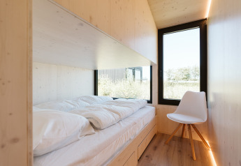 Habitación de madera luminosa con cama individual y silla blanca en Eden, Holiday park De Klepperstee, Países Bajos.