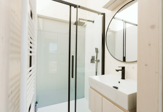 Baño moderno con ducha acristalada, grifería negra y espejo redondo en Eden lodge, De Klepperstee, Países Bajos.