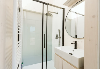 Salle de bain moderne avec douche en verre, robinet noir et miroir rond à l’Eden lodge, De Klepperstee, Pays-Bas.
