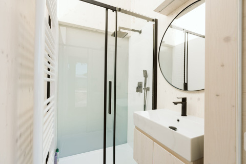 Moderne badkamer met glazen douche, zwarte kranen en rond spiegel in Eden-lodge, De Klepperstee, Nederland.