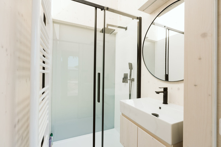 Baño moderno con ducha acristalada, grifería negra y espejo redondo en Eden lodge, De Klepperstee, Países Bajos.