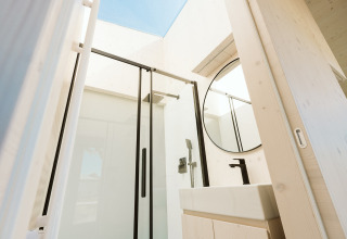 Moderne badkamer met glazen douche, ronde spiegel en dakraam in Eden lodge, Holiday park De Klepperstee.