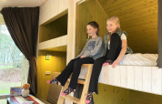 Twee meisjes zitten lachend op een hoogslaper in een Trek-in tiny house bij Beerze Bulten, Nederland.