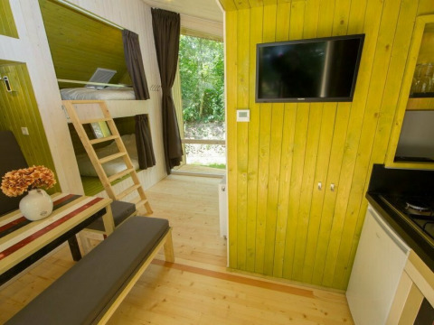 Interior de una tiny house Trek-in en Beerze Bulten, Países Bajos, con literas, mesa y televisor.
