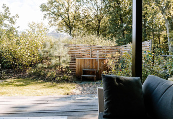 Blick von einer modernen Lodge mit Sofa auf privaten Garten, Holzzaun und Hot Tub bei Soof Retreats, Niederlande.