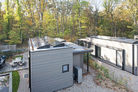 Moderne lodge in het bos met zonnepanelen op het dak, zitgedeelte en omringd door herfstbomen.