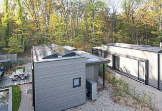 Moderne lodge in het bos met zonnepanelen op het dak, terras en omringd door kleurrijke herfstbomen.