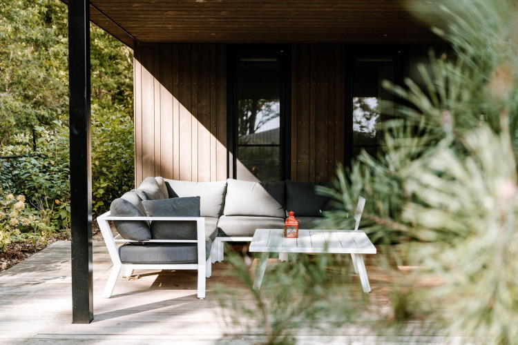 Cozy lodge patio with a modern gray sectional sofa and white table, surrounded by lush greenery and trees.