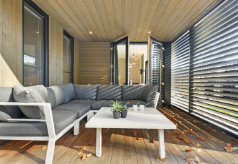 Moderne loungeområde på en lodge med grå sofa, hvidt bord og store vinduer, omgivet af træpaneler.