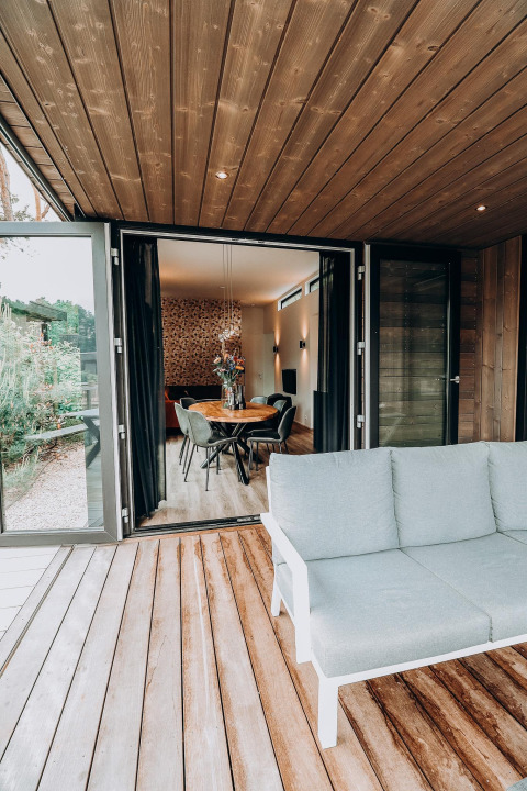 Terraza abierta de madera con sofá moderno y vista a un elegante comedor en el interior del lodge.