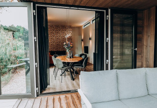 Open houten terras met moderne zetel en uitzicht op het eetgedeelte en het interieur van de lodge.