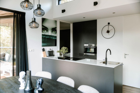 Moderne lodgekeuken met zwart-wit interieur, wandkunst, klok, kookeiland met spoelbak en grote ramen.