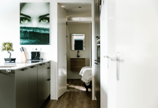 Moderne lodgekeuken met houtenvloer, kunst aan de muur en zicht op de slaapkamer in de achtergrond.