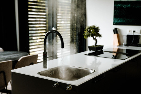 Moderne Küchenarmatur in einer Lodge mit heißem Wasser, Dampf, weißen Arbeitsflächen und einer Pflanze.