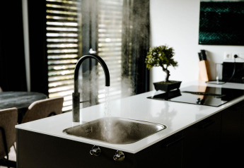 Moderno fregadero de cocina en un lodge con agua caliente, vapor, encimera blanca y planta verde.