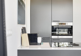 Cocina moderna en una cabaña con armarios grises, horno empotrado, bloque de cuchillos y encimera blanca.