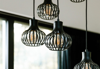 Lampade a sospensione moderne con struttura nera in un lodge, davanti a grandi finestre luminose.
