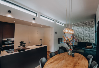 Moderne lodge met open keuken, ronde eettafel met bloemen en een gezellige zithoek met hoekbank.