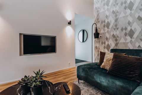 Salon moderne de lodge avec canapé vert, coussins décoratifs, télévision murale et plantes de table.