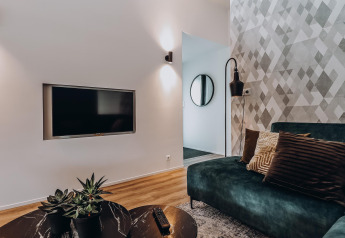 Moderne lodge woonkamer met groene bank, sierkussens, wand-tv, zwarte lamp en planten op tafel.