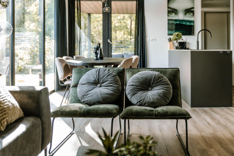 Salón moderno de lodge con sillas verdes, grandes ventanales y mesa de comedor al fondo.