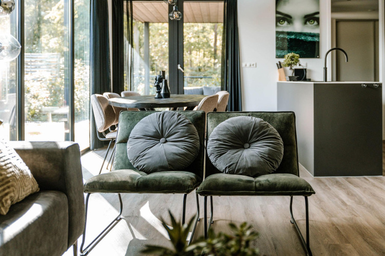 Modern lodge living room with green chairs, large windows, and a dining table in the background.