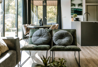 Salón moderno de lodge con sillas verdes, grandes ventanales y mesa de comedor al fondo.