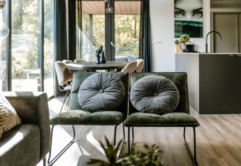 Moderne lodge zithoek met groene stoelen, grote ramen en een eettafel op de achtergrond.