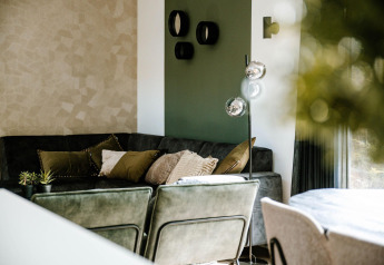 Soggiorno di lodge moderno con tonalità verdi e beige, cuscini accoglienti e piante decorative.