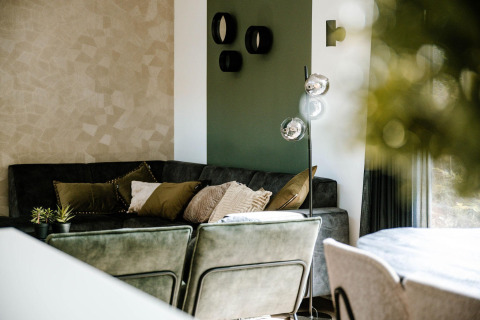 Sala de estar moderna en un lodge con tonos verdes y beige, cojines cómodos y una lámpara elegante.