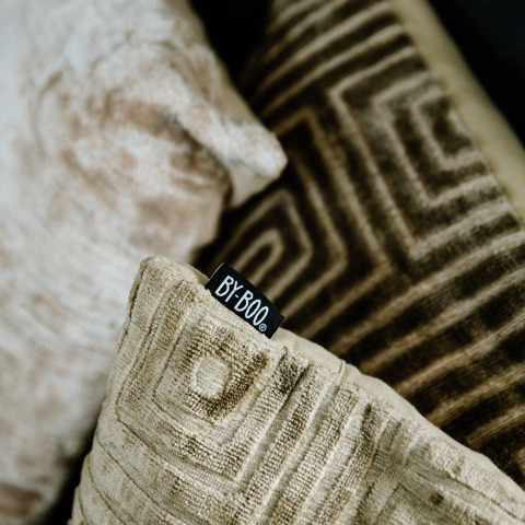 Dichtbijzicht van decoratieve kussens met geometrische patronen en zichtbaar BY-BOO-label in een lodge.