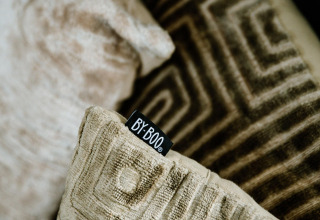 Close-up van decoratieve kussens met geometrische patronen en een zichtbaar BY-BOO-label in een lodge.