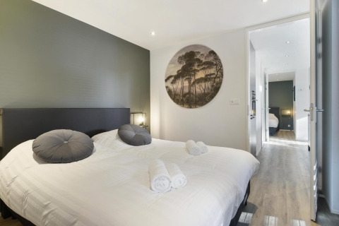 Dormitorio moderno de lodge con cama doble, dos cojines grises, arte mural y vista a otra habitación.