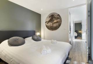 Modern lodge bedroom featuring a double bed, two gray pillows, wall art, and view into another room.