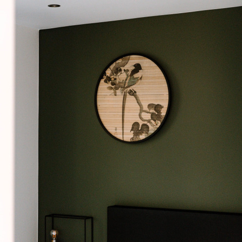 Un quadro rotondo con uccelli e rami è appeso a una parete verde scuro in una stanza di lodge moderna.