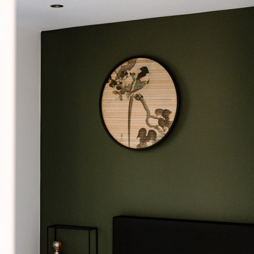 Una obra de arte redonda con pájaros y ramas cuelga de una pared verde oscura en una habitación de lodge.
