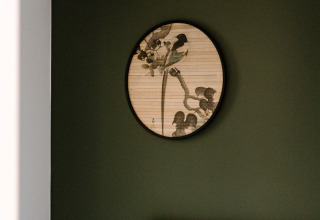 Een ronde decoratie met vogels en takken hangt aan een donkergroene muur in een stijlvolle lodgeruimte.