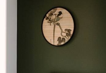 Una obra de arte redonda con pájaros y ramas cuelga de una pared verde oscura en una habitación de lodge.