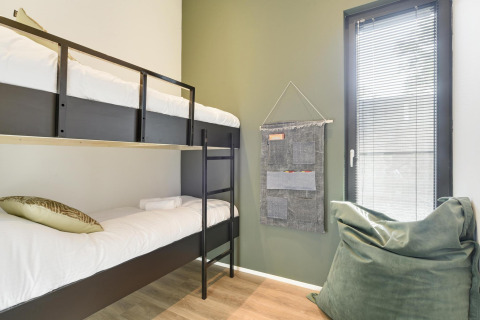 Habitación moderna en una cabaña con literas, pared verde, puff blando y ventana con persianas.