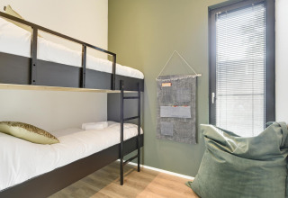 Moderne lodgekamer met stapelbedden, groene muur, zachte zitzak en raam met jaloezieën.