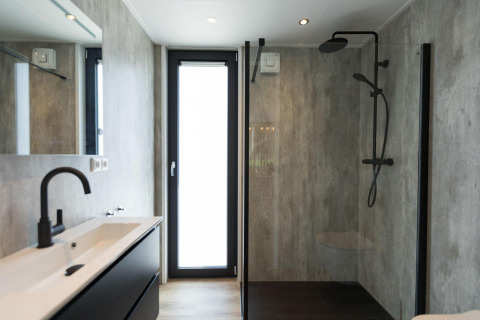 Bagno moderno in un lodge con doccia in vetro, rubinetteria nera e grande finestra luminosa.