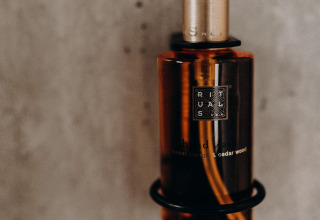 Dispenser ambrato Rituals fissato al muro in un lodge, con testo dell’etichetta visibile davanti.