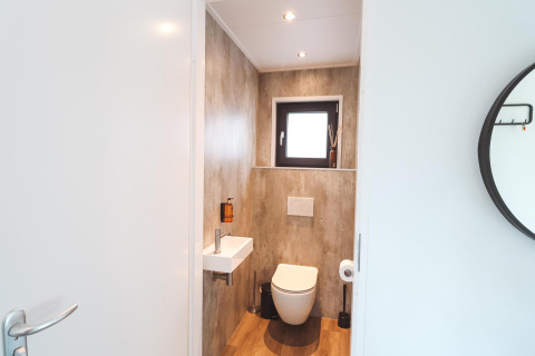 Baño moderno de lodge con inodoro suspendido, lavabo pequeño, ventana y decoración minimalista en madera.