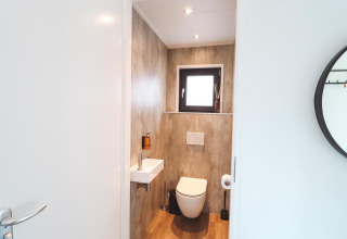 Baño moderno de lodge con inodoro suspendido, lavabo pequeño, ventana y decoración minimalista en madera.